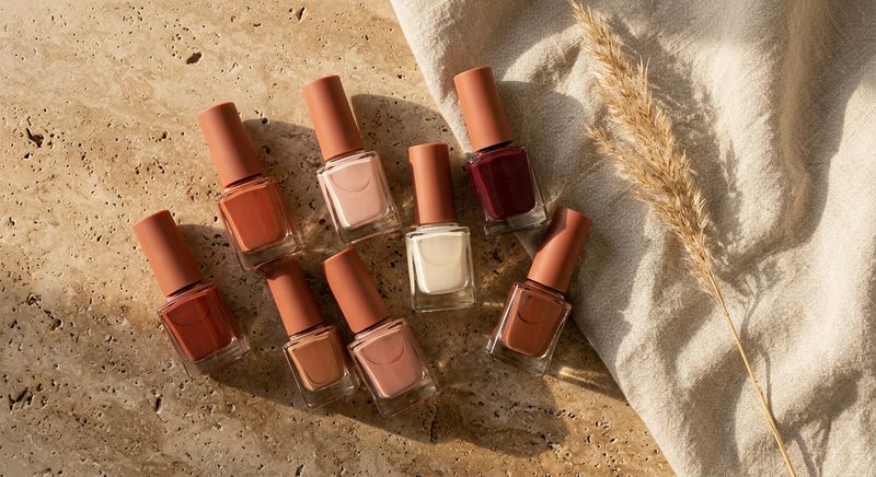 Terracotta, blush, and burgundy polish shades laid out on travertine stone